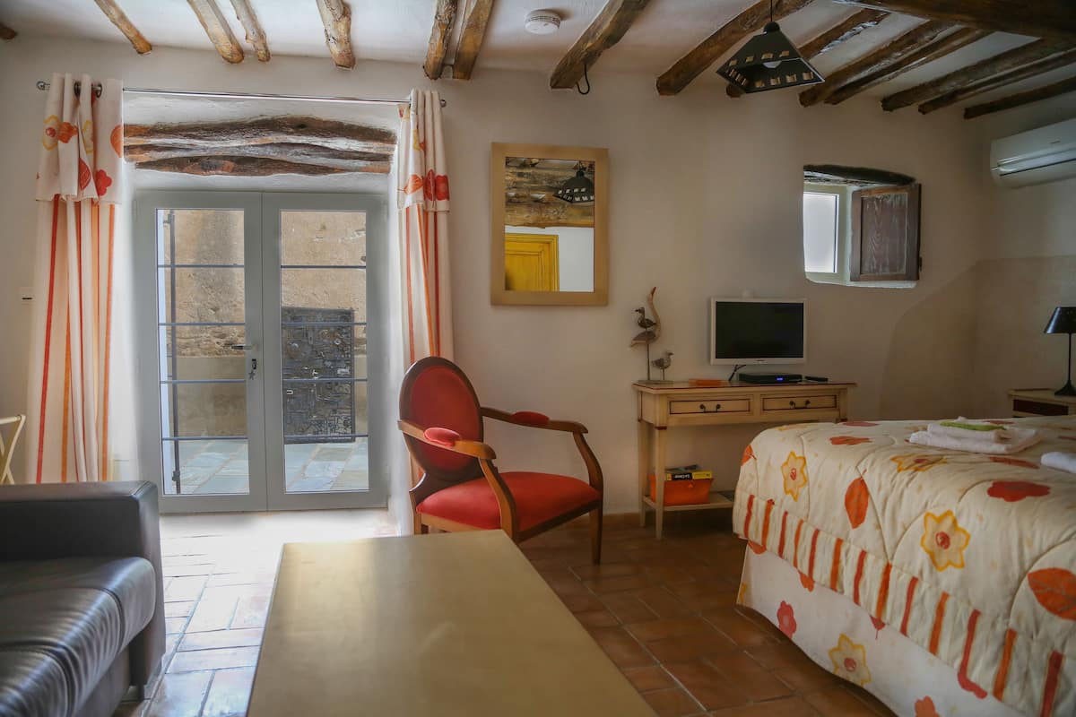 Een kamer met een bed, een bureau met een computer, een stoel, een bank en een schuifdeur naar een buitenruimte.
