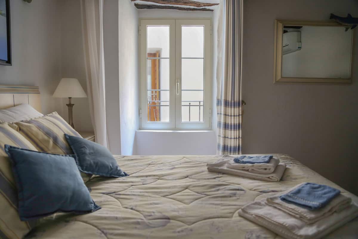 Een keurig opgemaakt bed met kussens, een lamp en een raam met gordijnen.