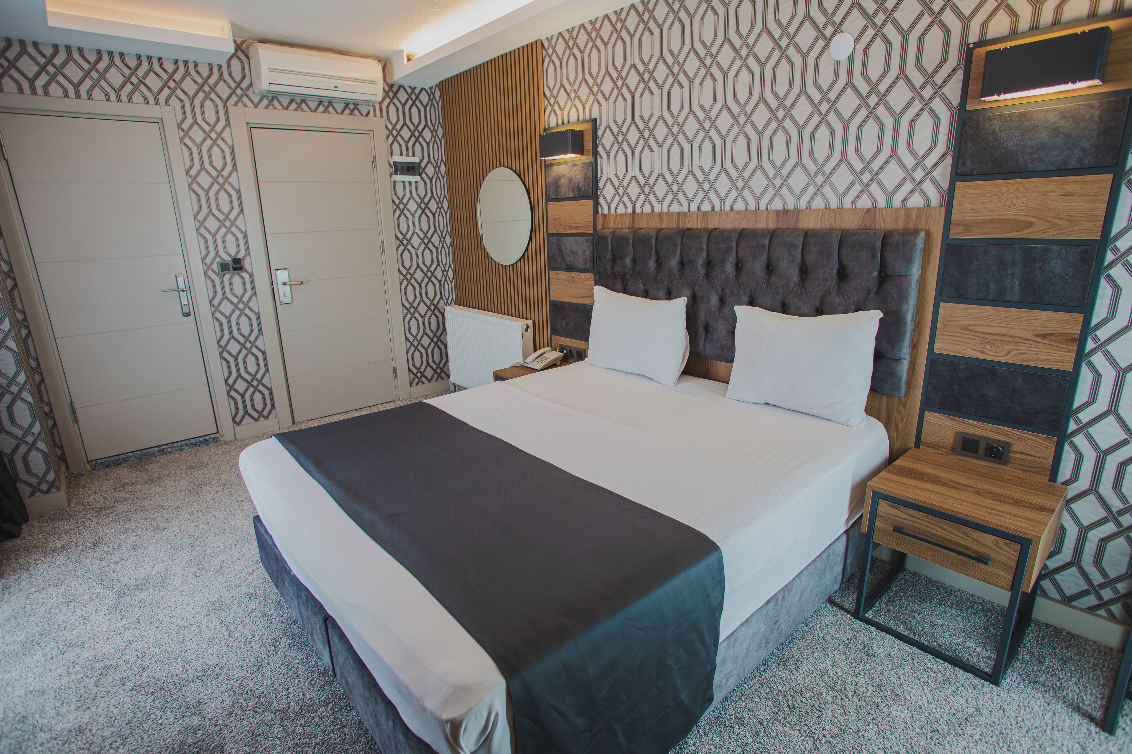 A hotel room with a large bed, a bedside table, a nightstand, a mirror, and a wardrobe.