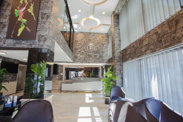 A hotel lobby with a reception desk, seating area, and large windows. - Prusias Otel (Bursa)