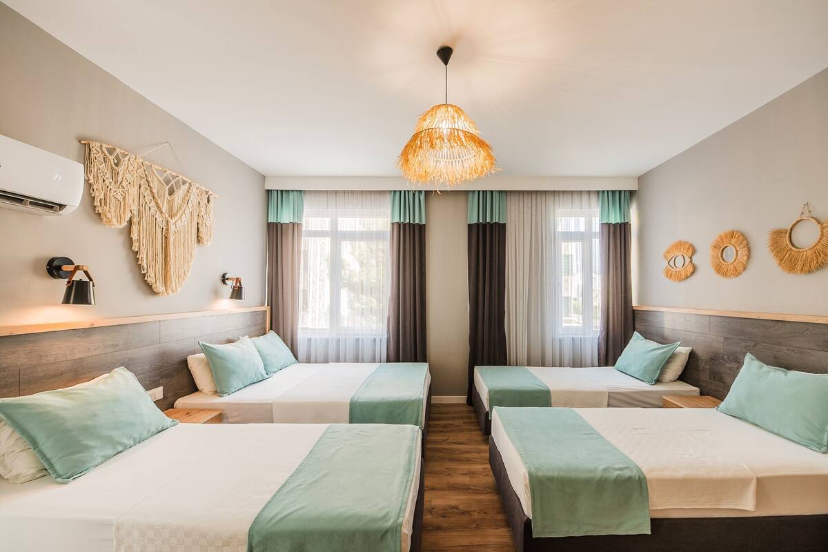 Quarto de hotel com duas camas, uma decoração de tapeçaria pendurada na parede, um ventilador de teto e um ar condicionado fixado na parede.