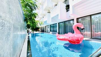 A swimming pool with a pink flamingo float, surrounded by modern buildings with balconies and large windows.