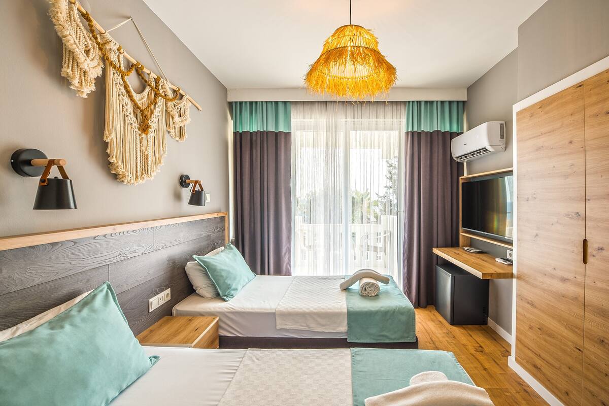 Quarto de hotel moderno com cama, mesas de cabeceira, escrivaninha, televisão e guarda-roupa.