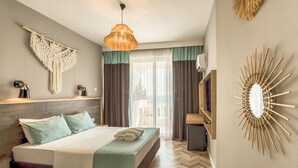 A modern hotel room with a bed, a hanging macrame wall decoration, a ceiling fan, and a large mirror with a sunburst frame. - Royal City Hotel (Antalya)