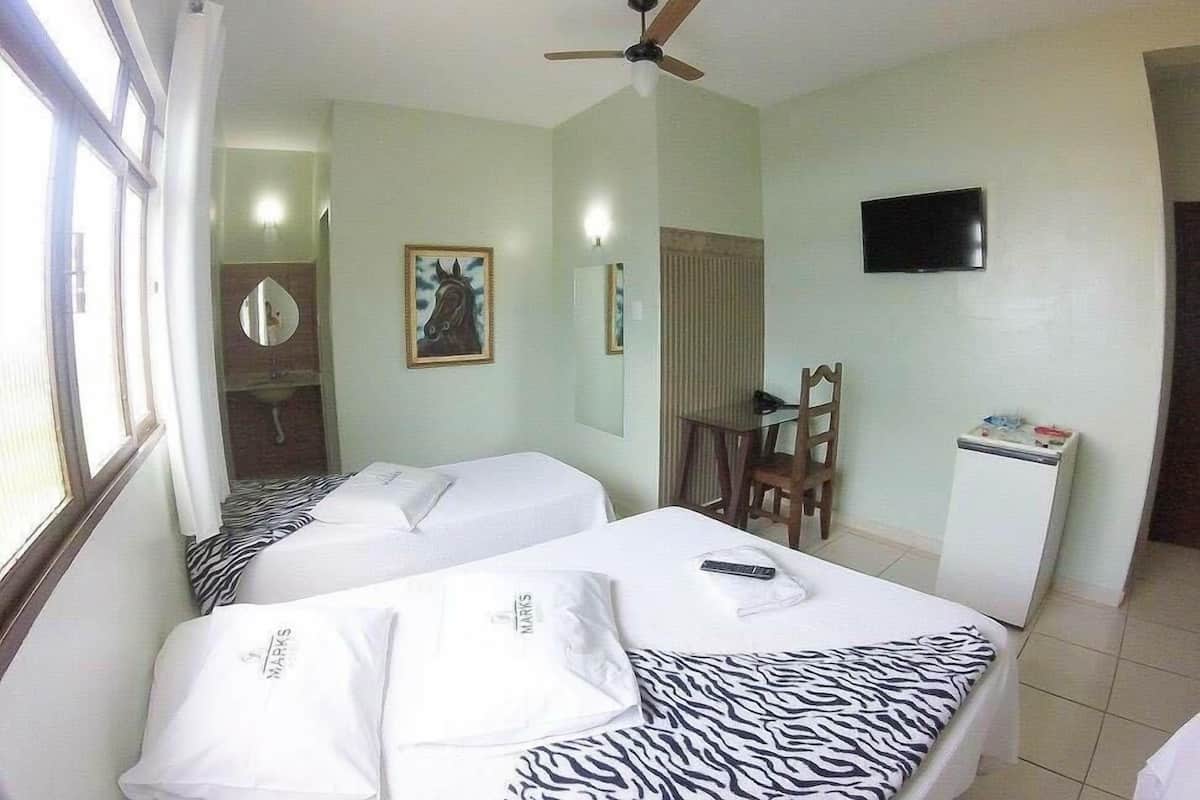 A hotel room with two beds, a ceiling fan, a TV on the wall, and a small table with a chair.