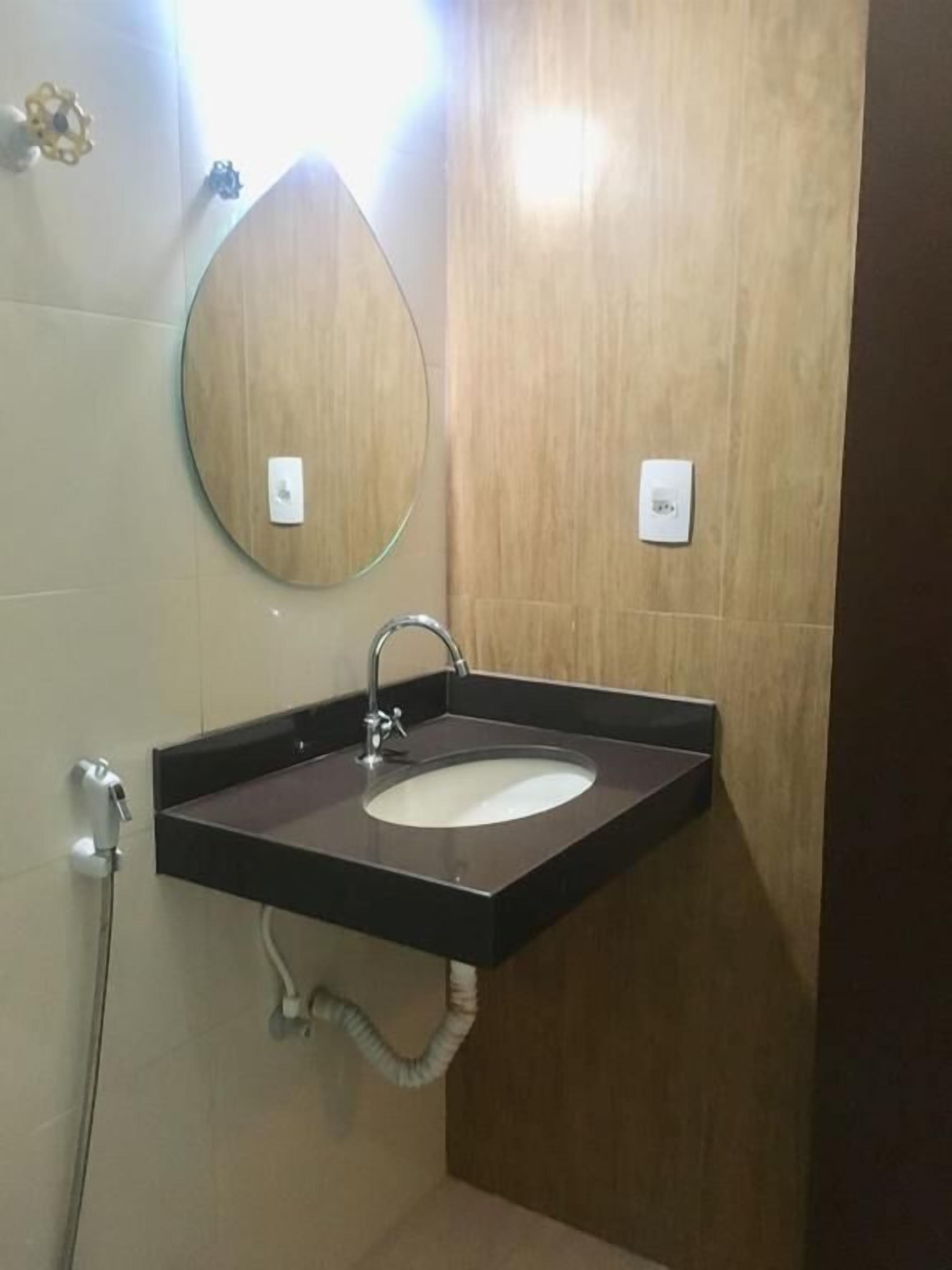 Casa de banho com uma pia retangular, um espelho redondo e um porta-toalhas.