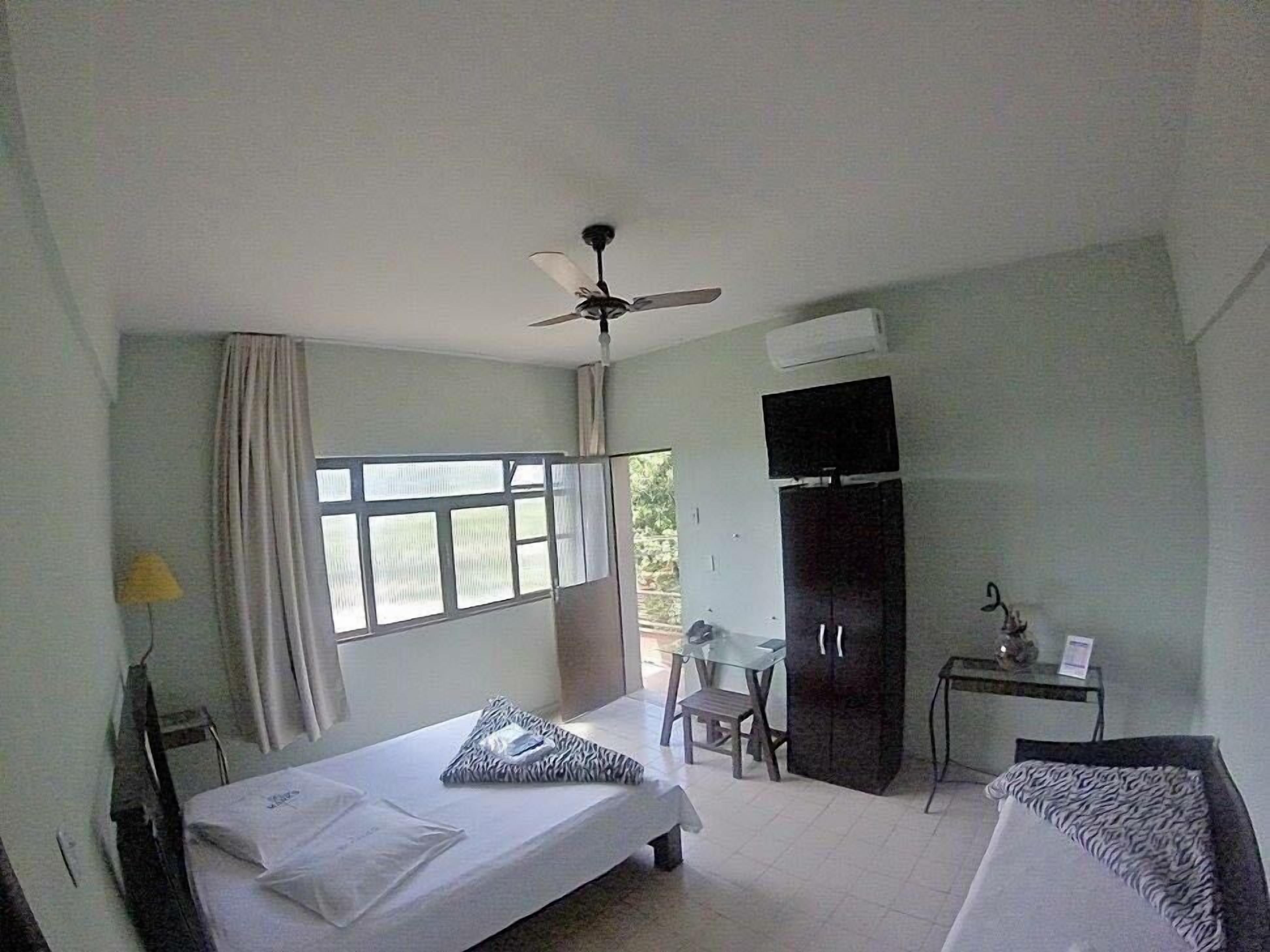 A bedroom with a bed, a desk, a chair, a wardrobe, and a ceiling fan.