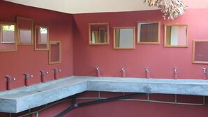 Casa de banho com várias pias e espelhos numa parede vermelha.