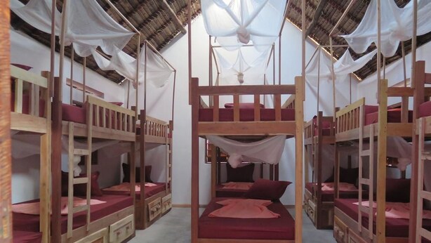 Um quarto com beliches dispostos em formato de U, cada um com estrutura de madeira e roupa de cama vermelha.
