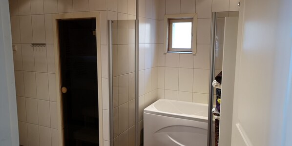 Un baño con bañera, ducha y un ventanal pequeño.