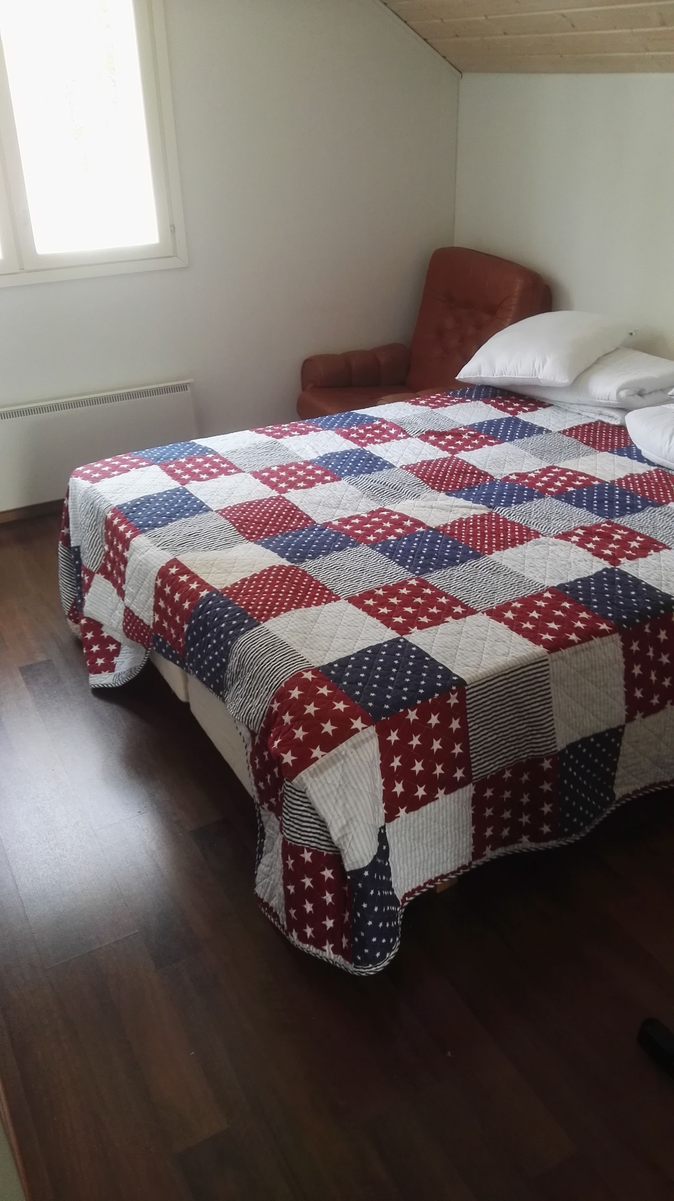 A bedroom with a bed covered by a red, white, and blue quilt.