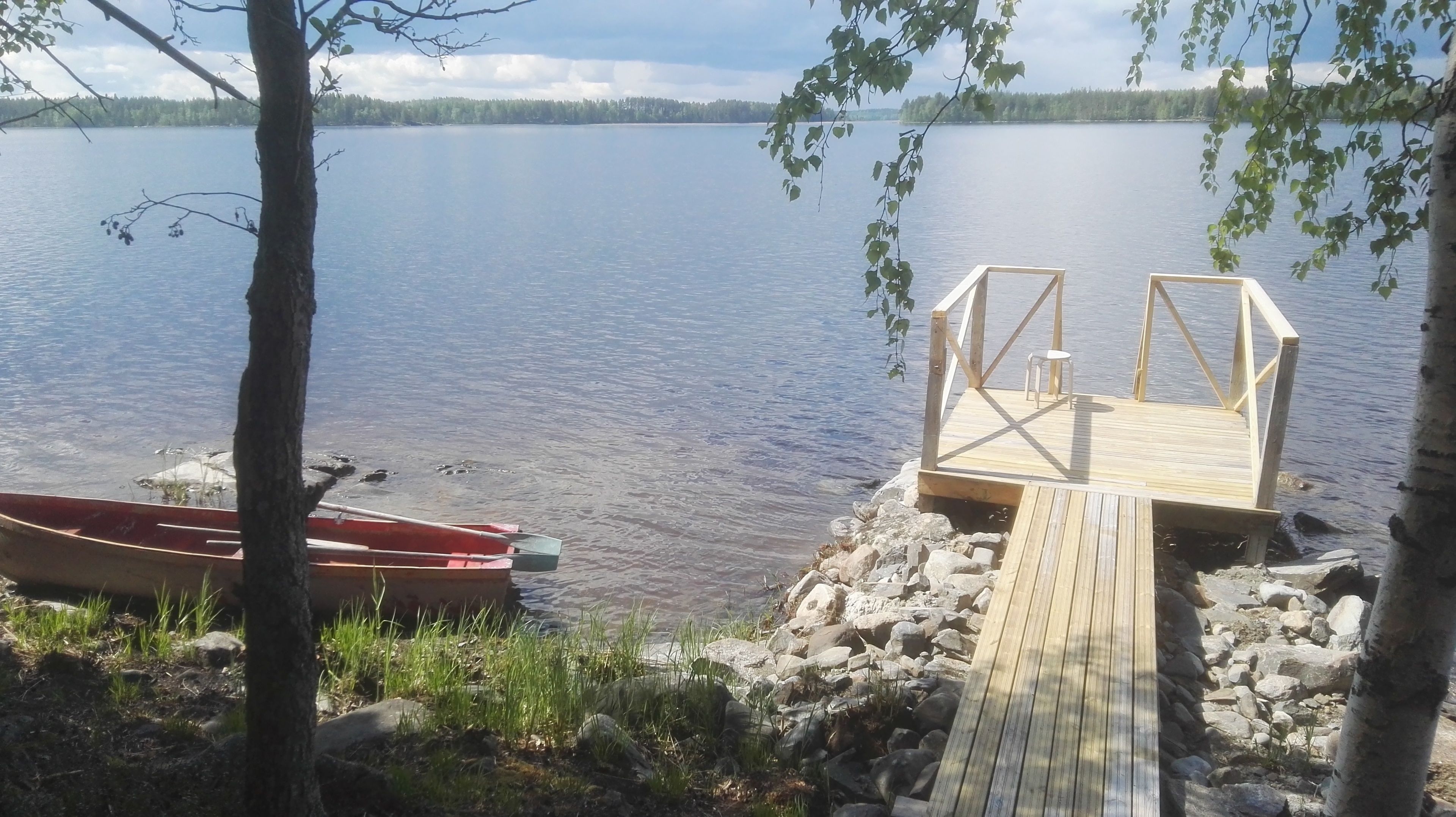 A wooden dock leading to a small wooden pier with a bench and a chair.