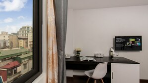 Una habitación moderna con un ventanal grande, un escritorio con silla, un televisor de pantalla plana y un mueble bajo.