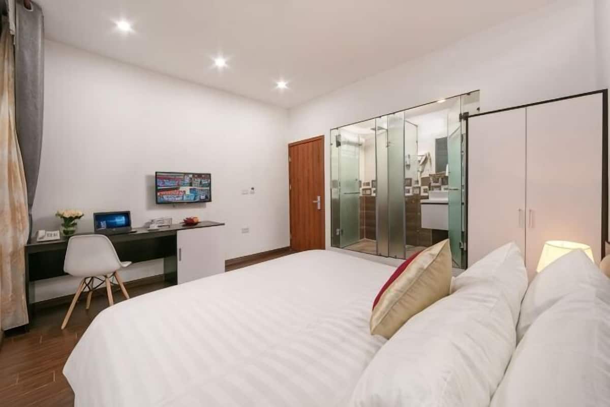 A bedroom with a bed, a desk with a computer, a TV, and a wardrobe.