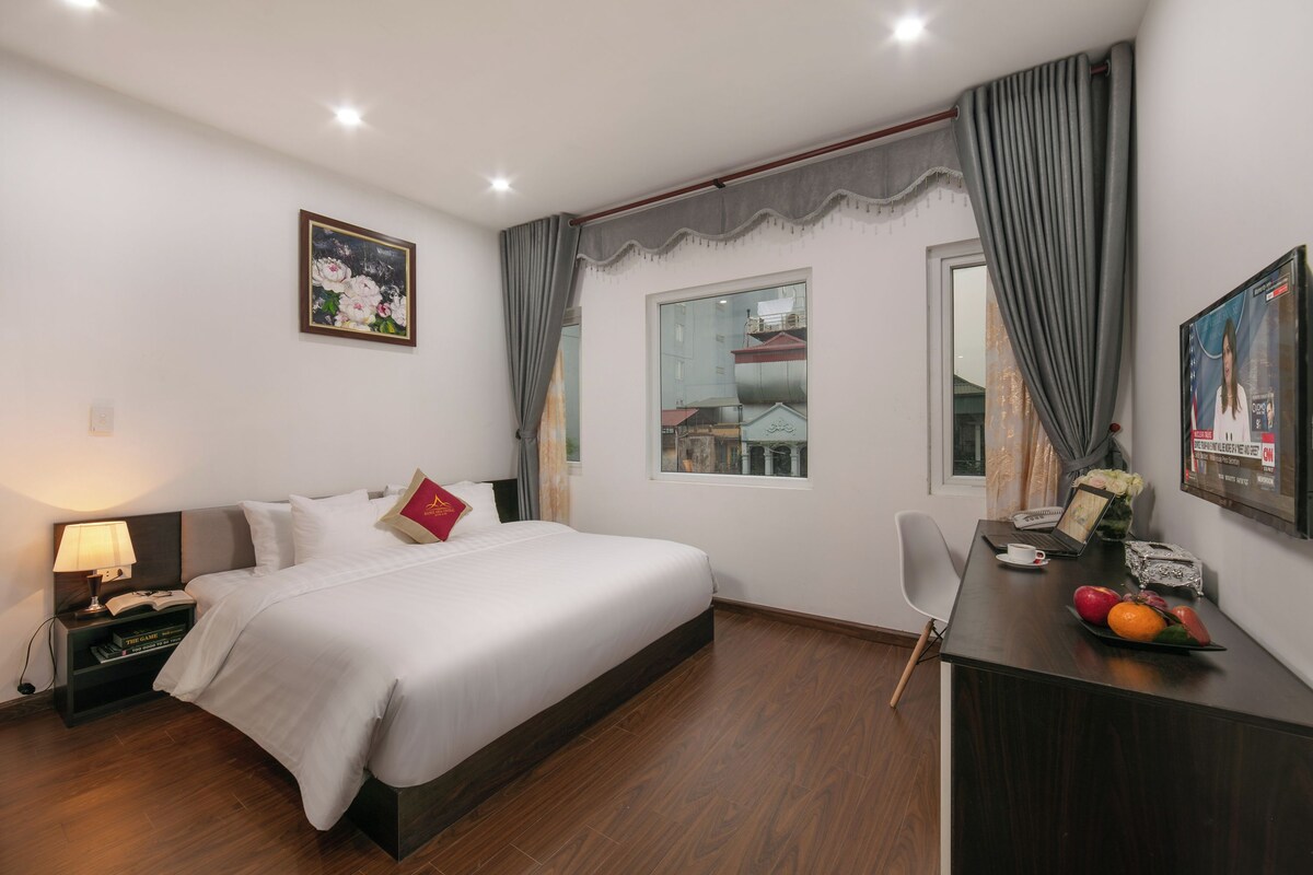 Une chambre d’hôtel comprenant un lit, un bureau avec un ordinateur portable, une chaise, une table de chevet avec une lampe et une fenêtre avec des rideaux.