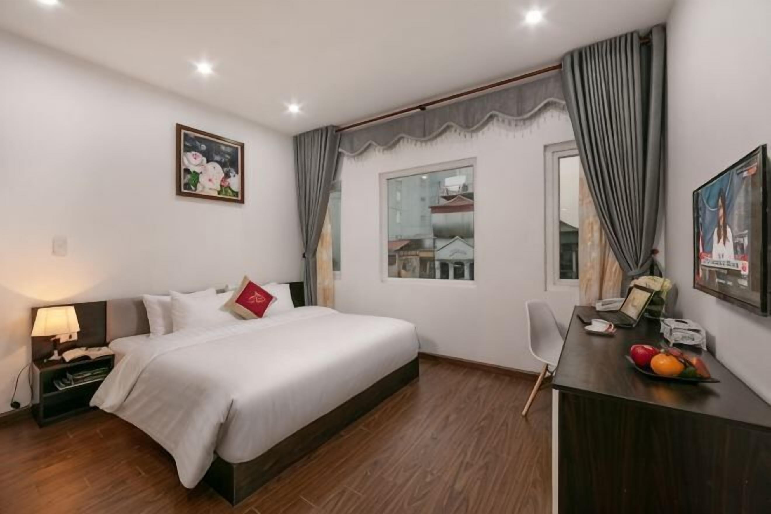 Ein Hotelzimmer mit Bett, Schreibtisch, Stuhl und einem fenster mit Vorhängen.
