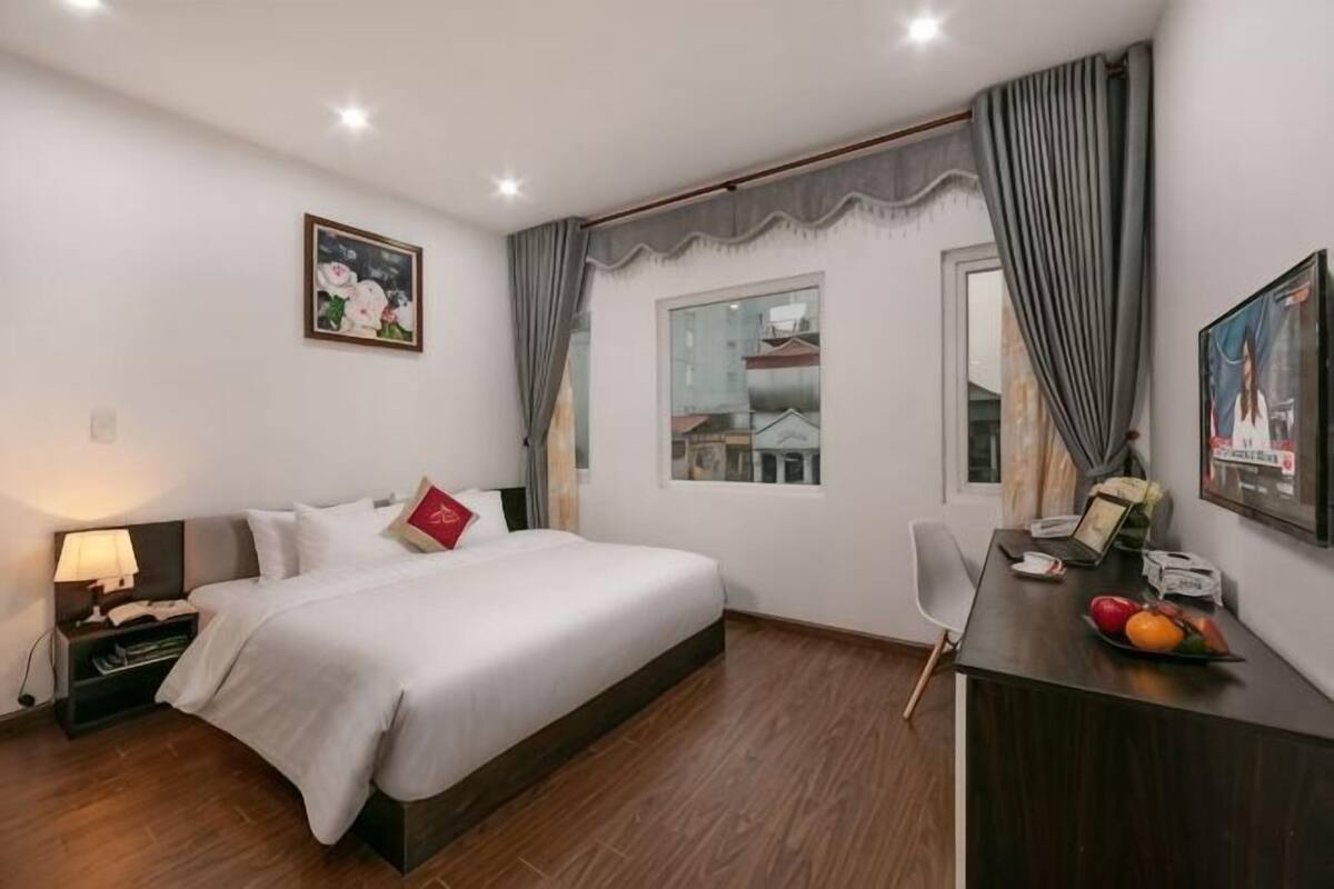 A hotel room with a bed, desk, chair, and a window with curtains.