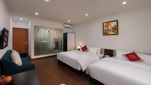 Habitación de hotel con dos camas, un sofá, una puerta de madera, un separador de vidrio y un cuadro en la pared.