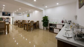 Un área de comedor moderna con mesas y sillas de madera, una planta grande en maceta y un bufé con diversos platos.