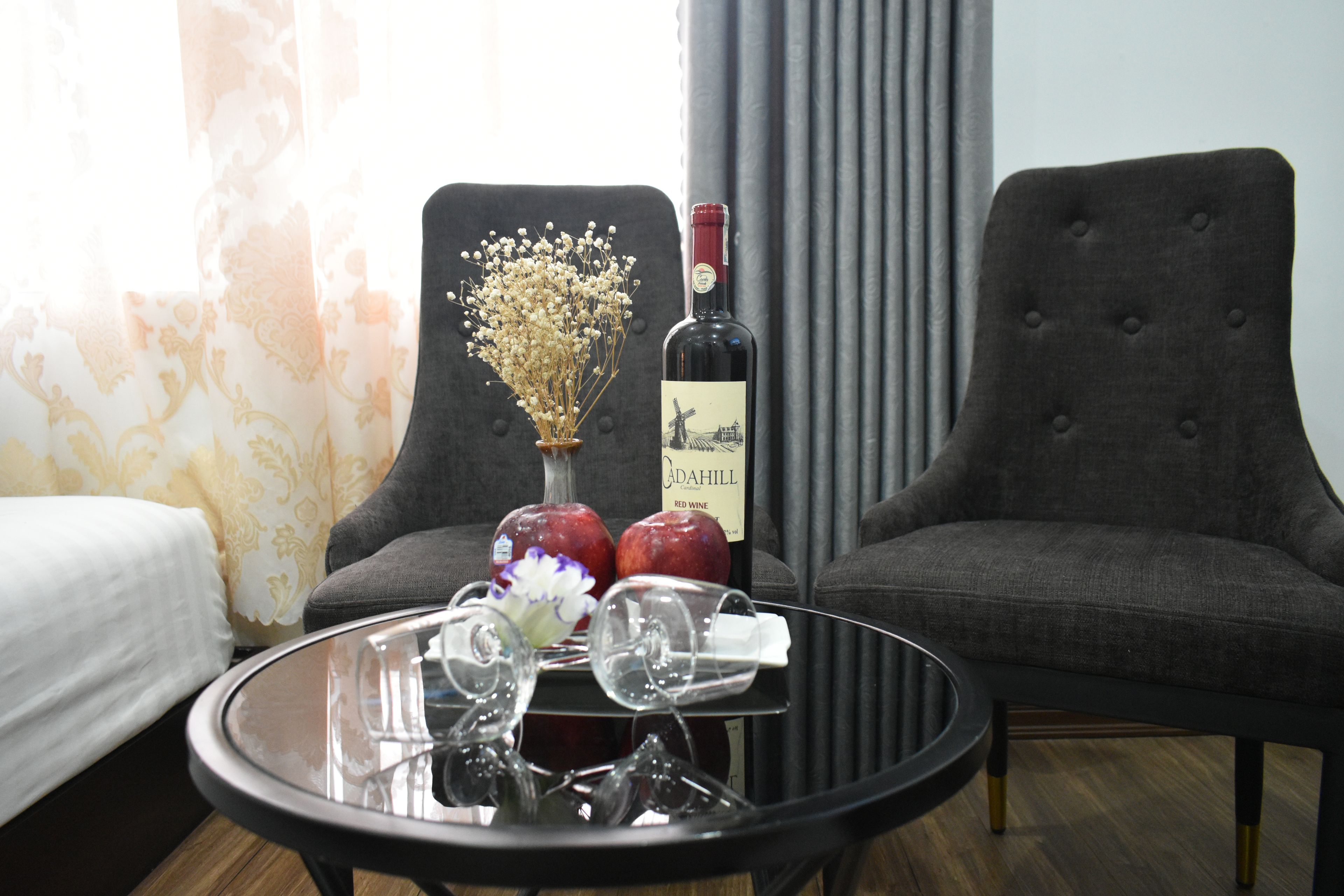 Una habitación con una cama, una mesa redonda con copas de vino y una botella, y dos sillones.