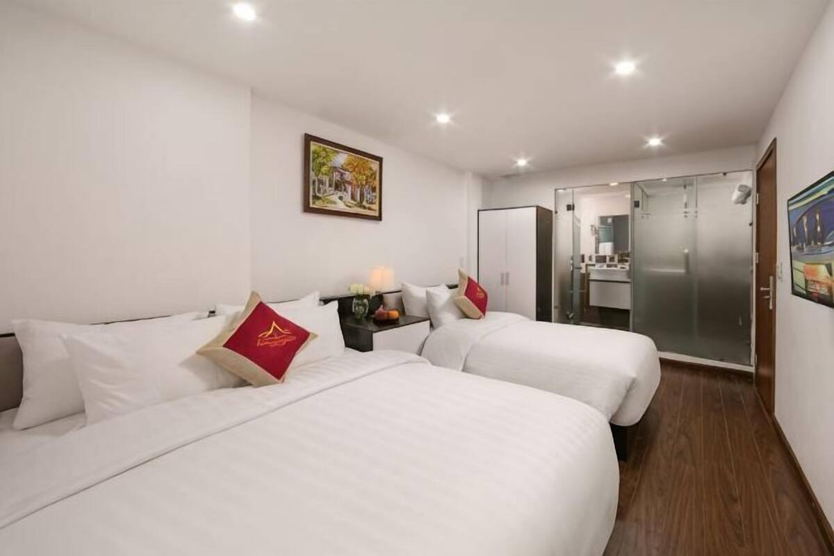 A hotel room with two beds, a small table with a lamp, a mirror, and a wardrobe.