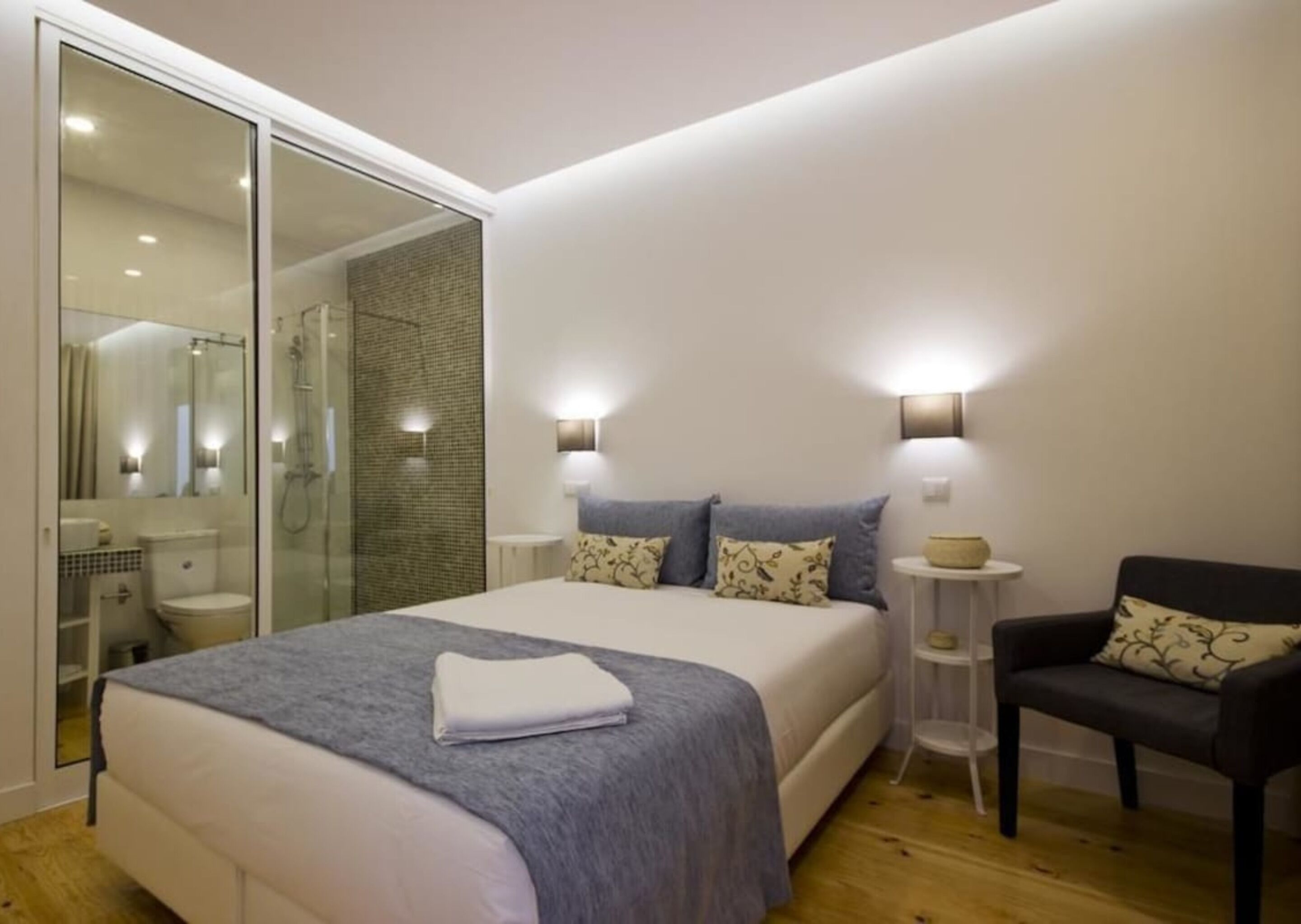 A modern bedroom with a large bed, a glass shower enclosure, and a small bedside table.