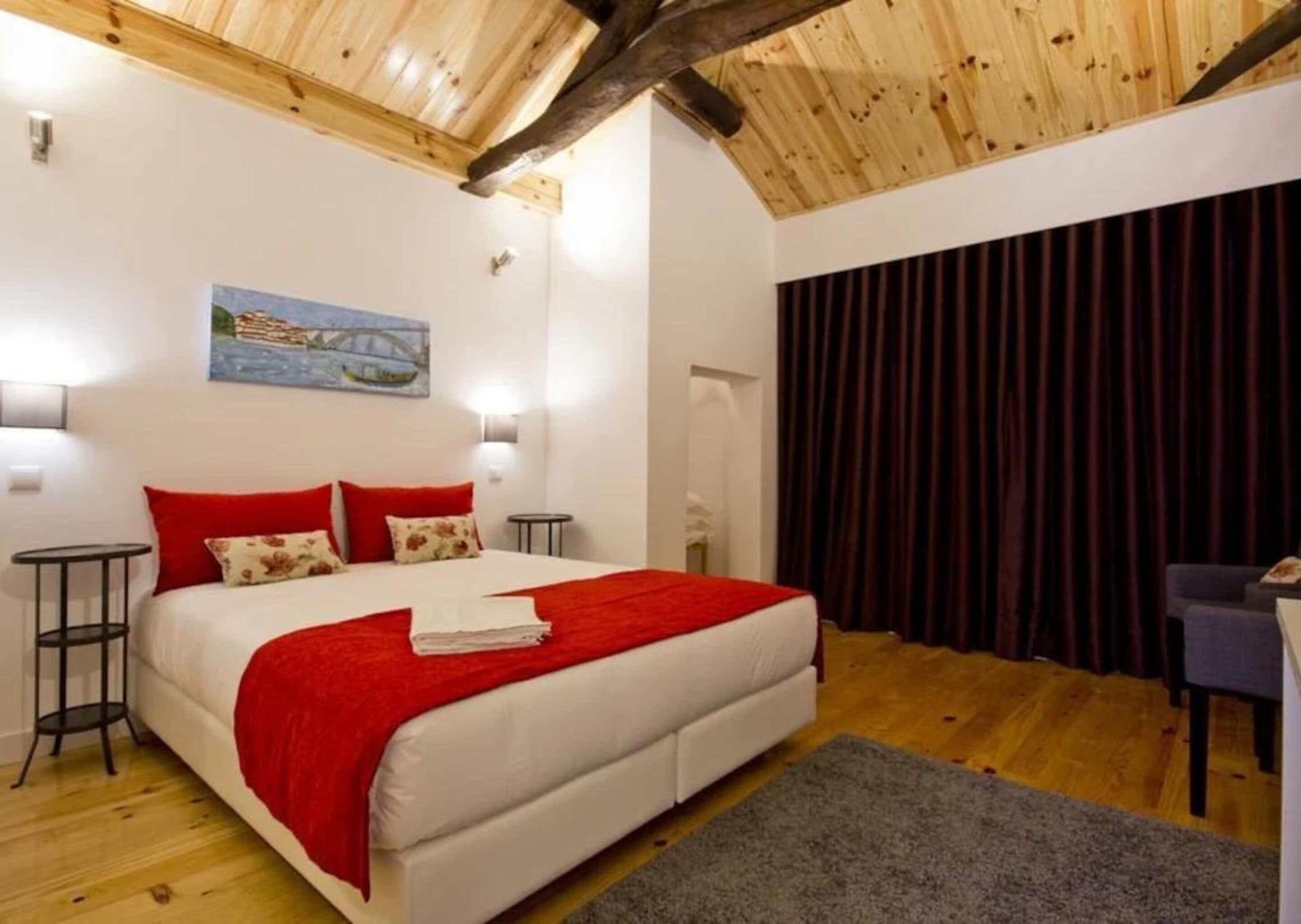 Une chambre avec un grand lit, une literie rouge, un tableau au mur et un plafond en bois.