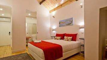 A bedroom with a wooden ceiling, a bed with red and white bedding, a painting on the wall, and a small bedside table.