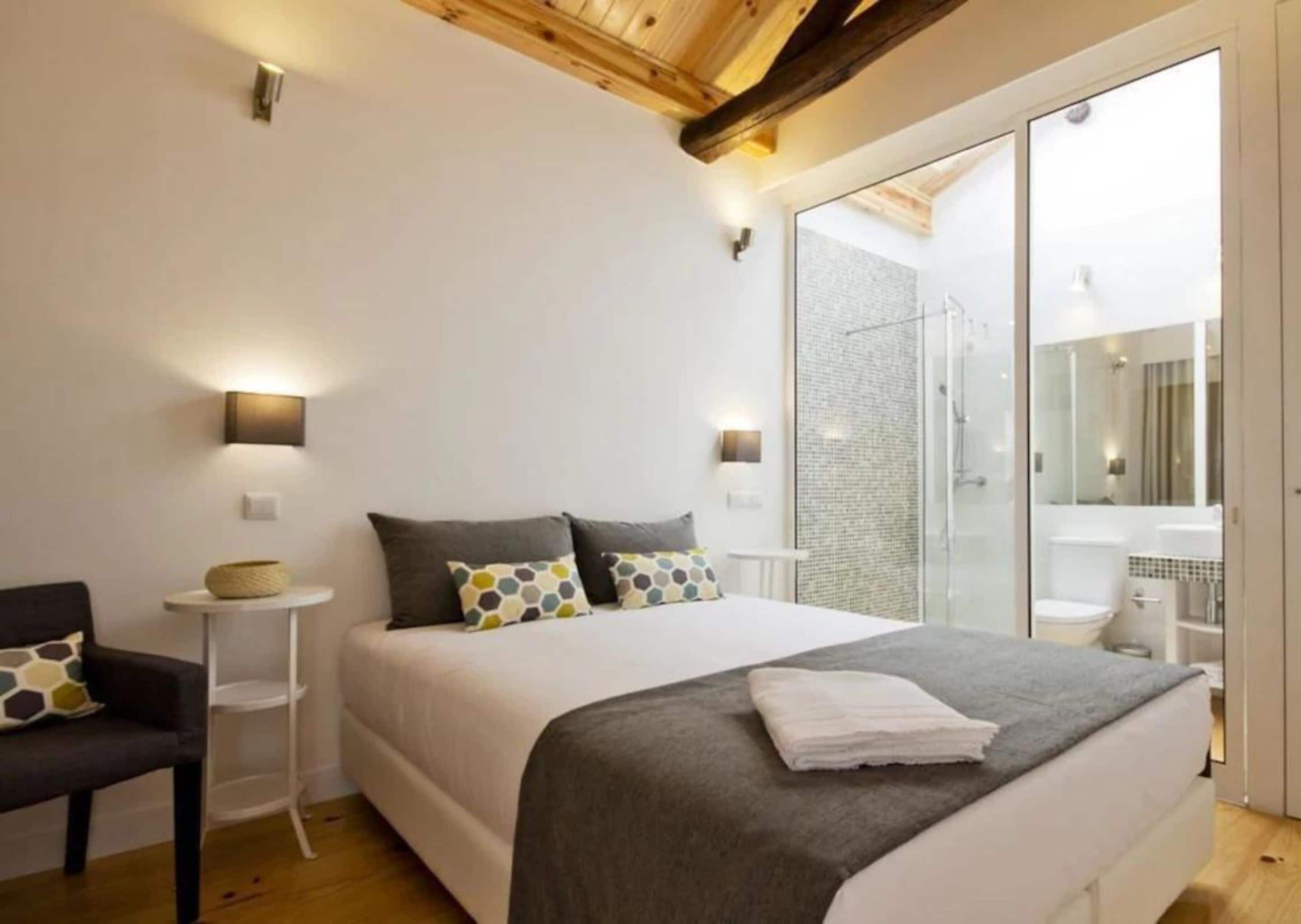 Un dormitorio moderno con una cama grande, mesitas de noche, una silla y una zona de ducha con mampara de vidrio.