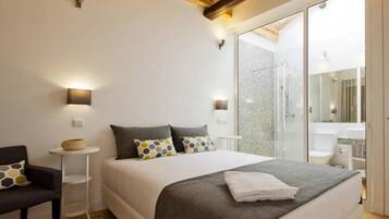 Un dormitorio moderno con una cama grande, mesitas de noche, una silla y una zona de ducha con mampara de vidrio.
