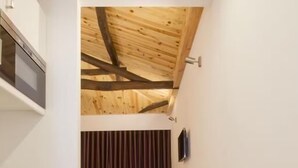 A narrow hallway with wooden flooring, a kitchen area on the left, and a dining area with a table and chairs in the background. - MyStay Porto Bolhão (Porto)