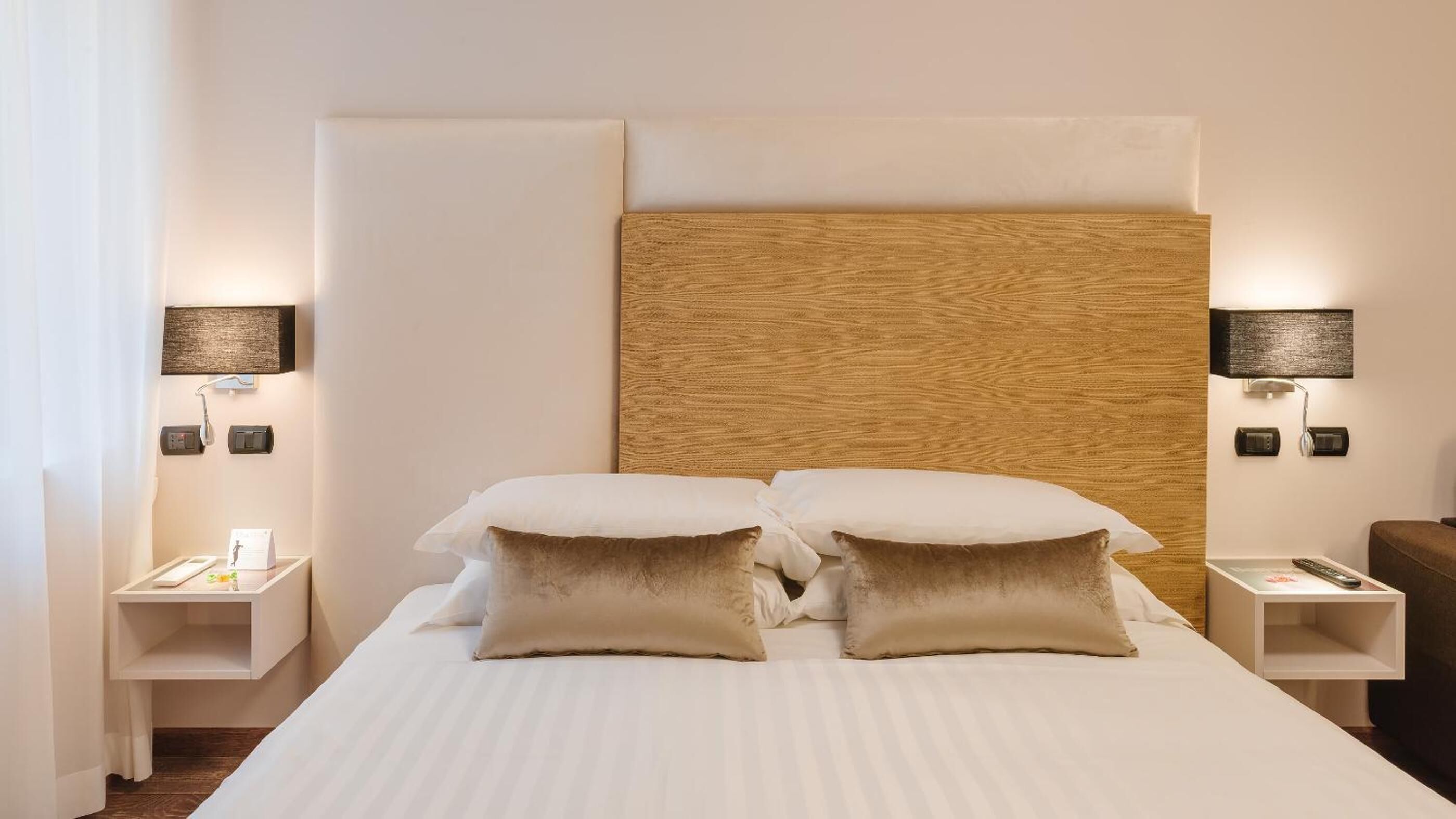 A hotel room with a large bed, two bedside tables, a wooden headboard, and wall-mounted lamps.