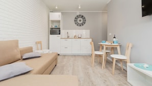 A modern, compact living space with a kitchenette, a dining area, and a sofa with cushions. - Villa Ula Apartament (Rewal)