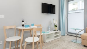 A modern living room with a flat-screen TV, a dining table with chairs, a small glass table, and a sofa. - Villa Ula Apartament (Rewal)