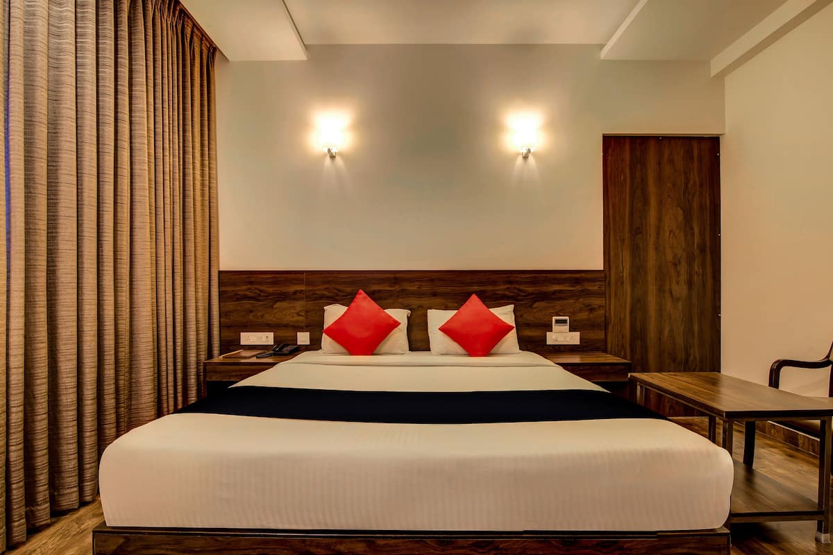 A hotel room with a large bed, two bedside tables, a wooden headboard, and a desk with a chair.