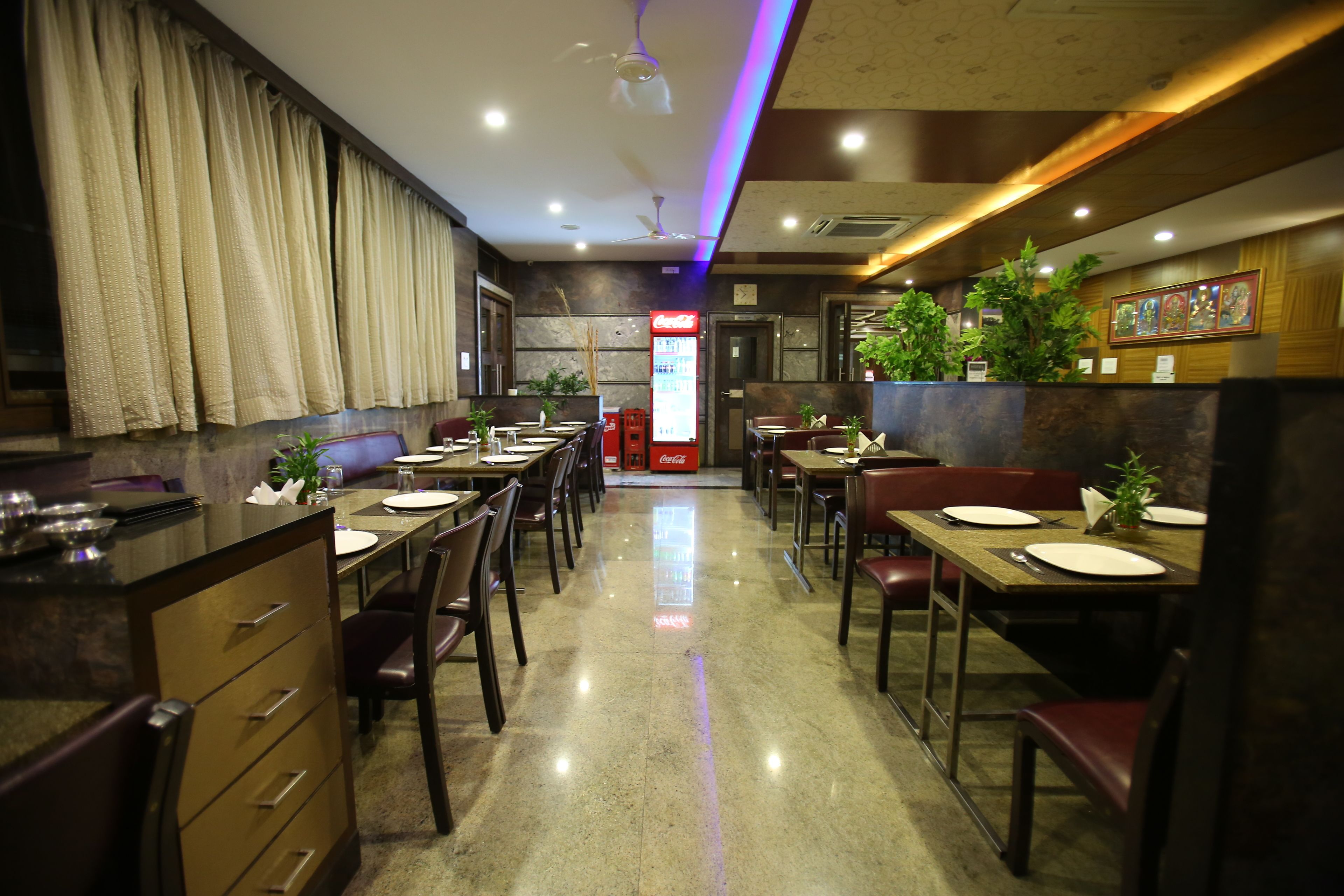 A restaurant with multiple tables and chairs, a Coca-Cola refrigerator, and potted plants.