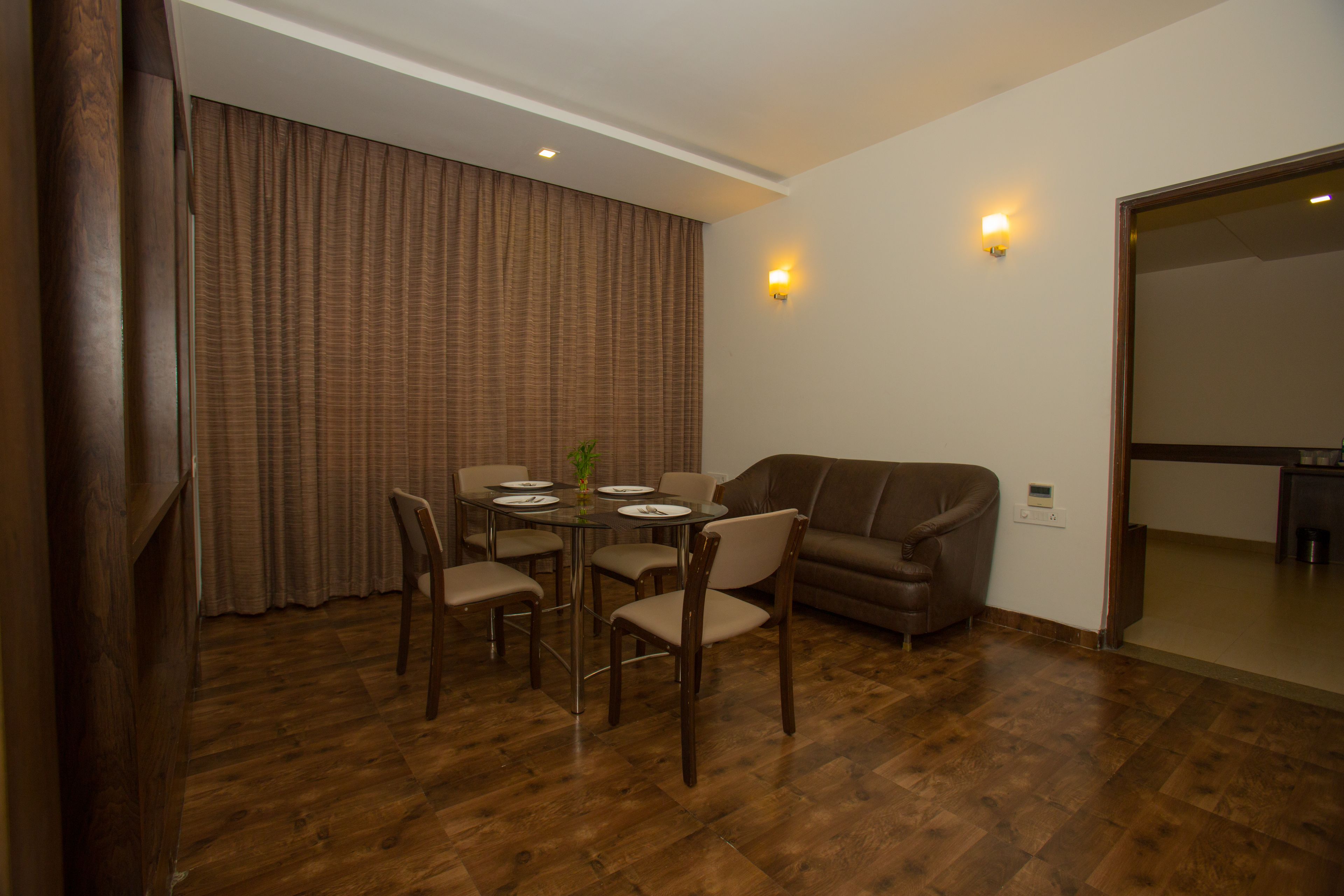 A dining area with a round table, four chairs, a sofa, and a wall-mounted light fixture.