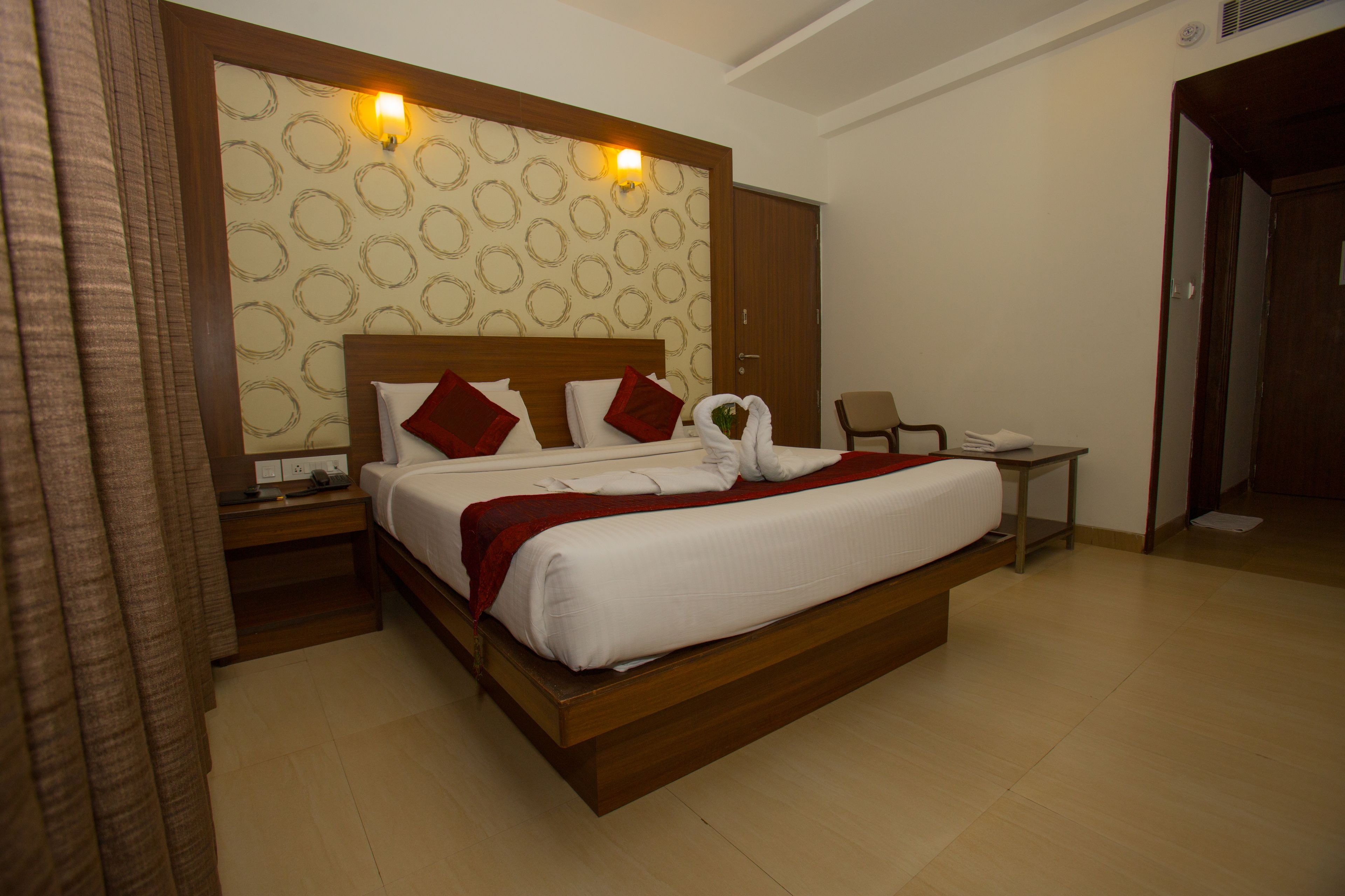 A hotel room with a large bed, a wooden headboard, a nightstand, a desk, and a chair.