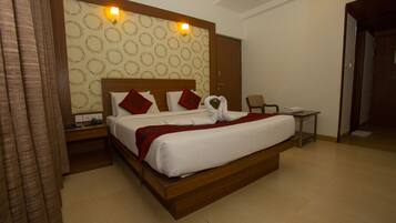 A hotel room with a large bed, a wooden headboard, a nightstand, a desk, and a chair.