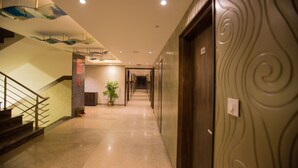 Un pasillo de hotel con suelo de mármol, una escalera a la izquierda y una puerta de madera a la derecha.