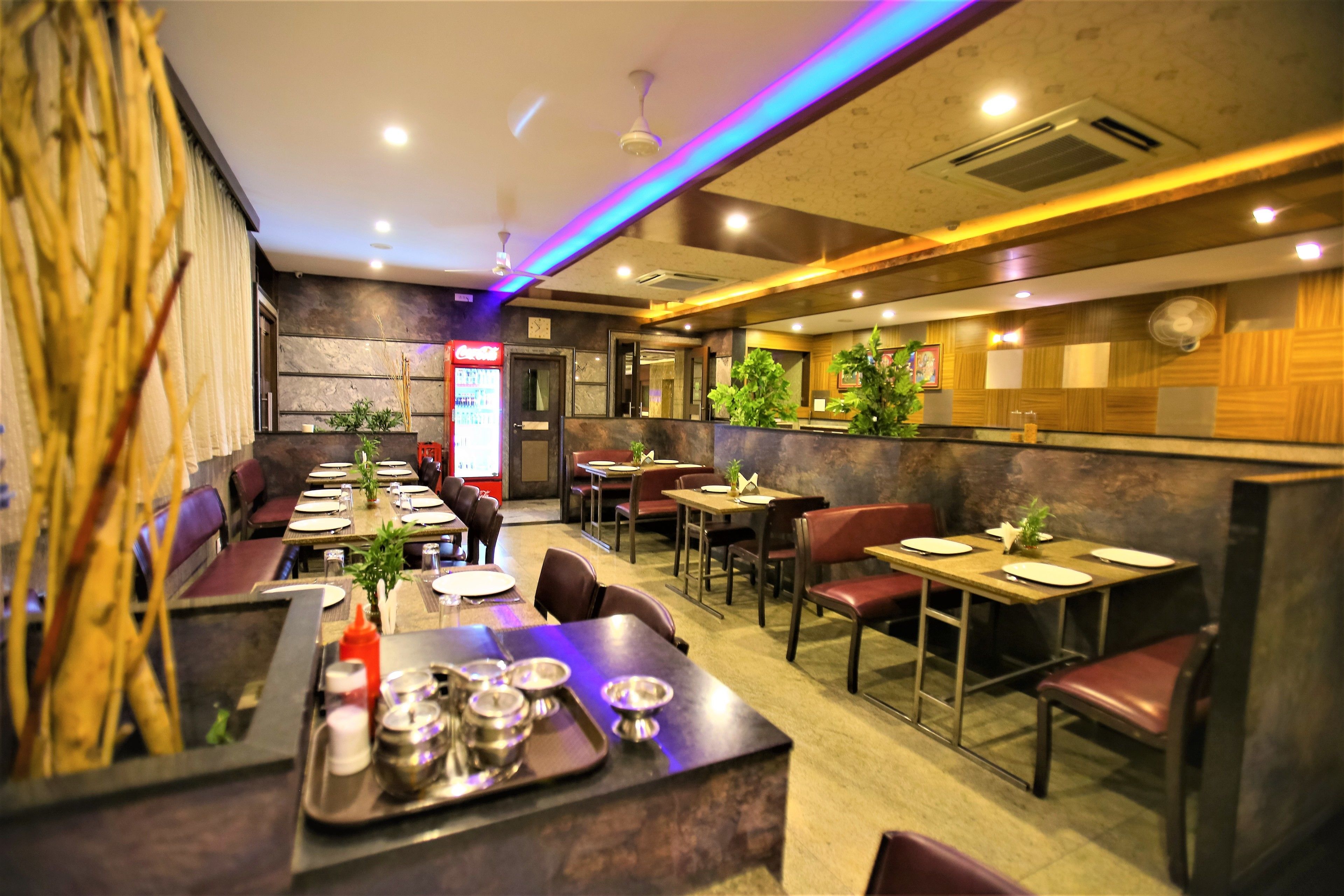 A restaurant interior with booths and tables, some with plants, and a counter with trays and utensils.