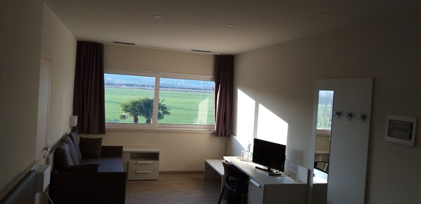 A hotel room with a large window, a desk, a chair, a small cabinet, and a bed. - Albergo Alla Campagna (Trissino)