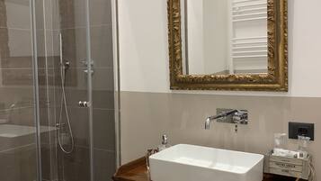 Une salle de bain dotée d’une douche à parois de verre, d’un lavabo blanc, d’un meuble-lavabo en bois et d’un grand miroir avec un cadre orné.