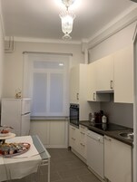 A compact kitchen with white cabinets, a built-in oven, a refrigerator, and a dining table with a clear glass top.