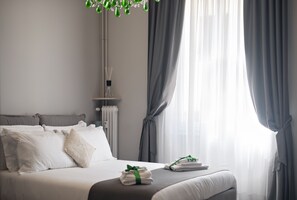 Una cama bien hecha con ropa blanca y una toalla verde, cortinas grises y un radiador en una habitación de hotel moderna.