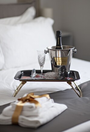 A bed with a tray holding a bottle of champagne, a glass, and a folded towel. - Il Genovino (Genoa)