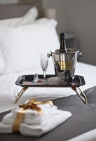 A bed with a tray holding a bottle of champagne, a glass, and a folded towel.