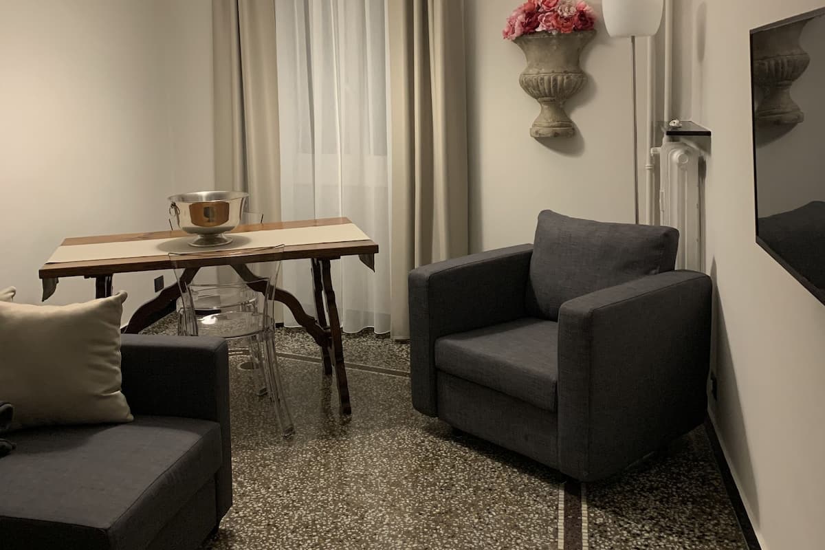 A compact living space with a sofa, a dining table, a chair, a floor lamp, and a wall-mounted TV.