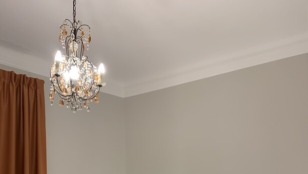 A neatly made bed with a brown headboard, a bedside table with a lamp, and a chandelier. - Il Genovino (Genoa)