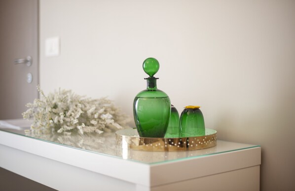 Un tocador de baño con una superficie de vidrio, una botella verde y un adorno blanco.